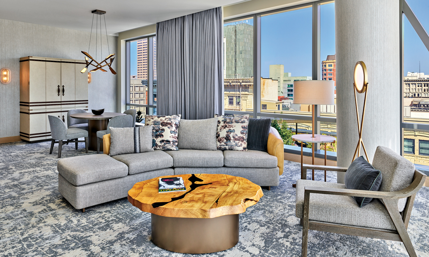 Ritz-Carlton suite with curved gray sofa and armchair around a wood coffee table in front of a wall of windows