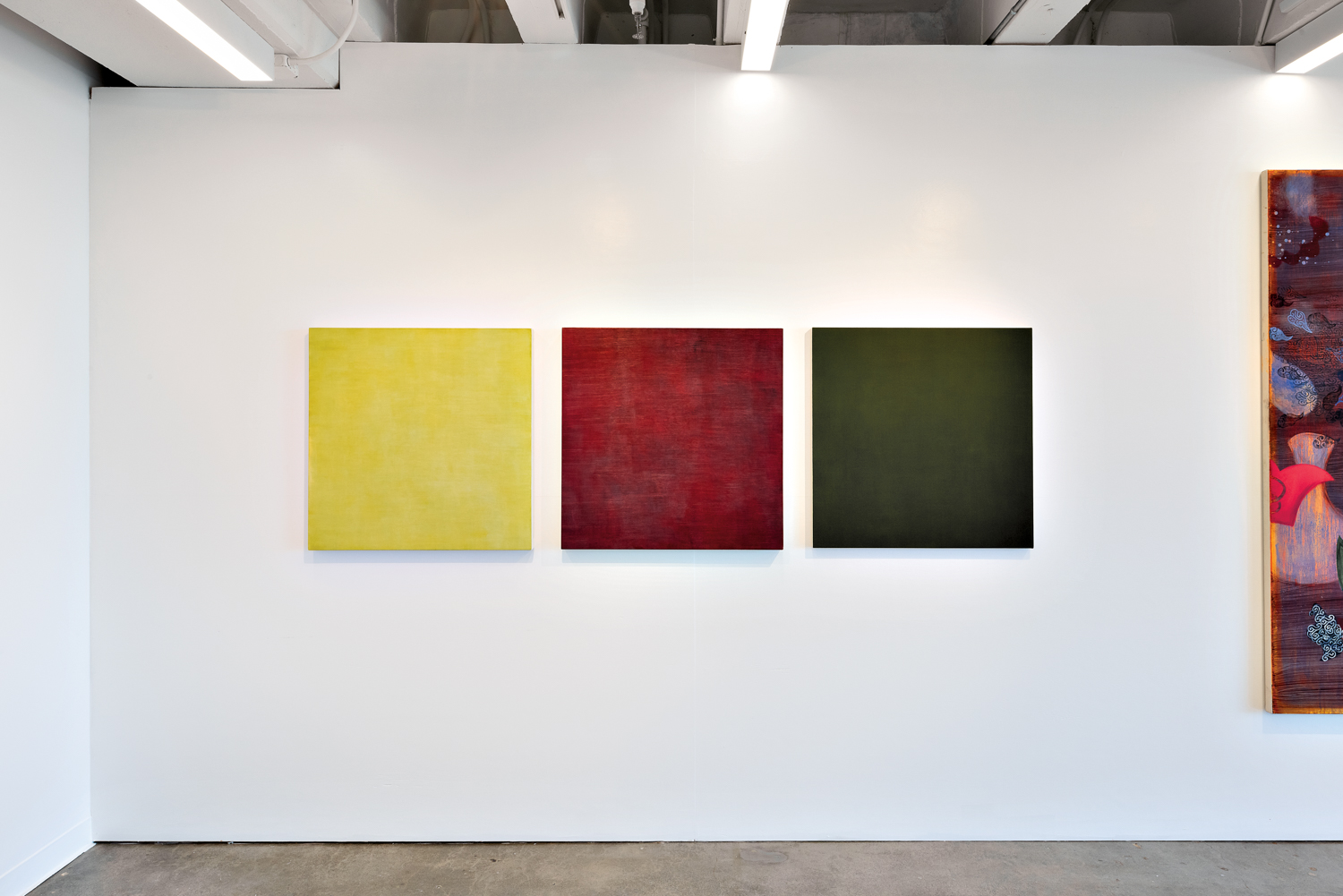 Three square artworks (one yellow, one red and one green) against a white wall