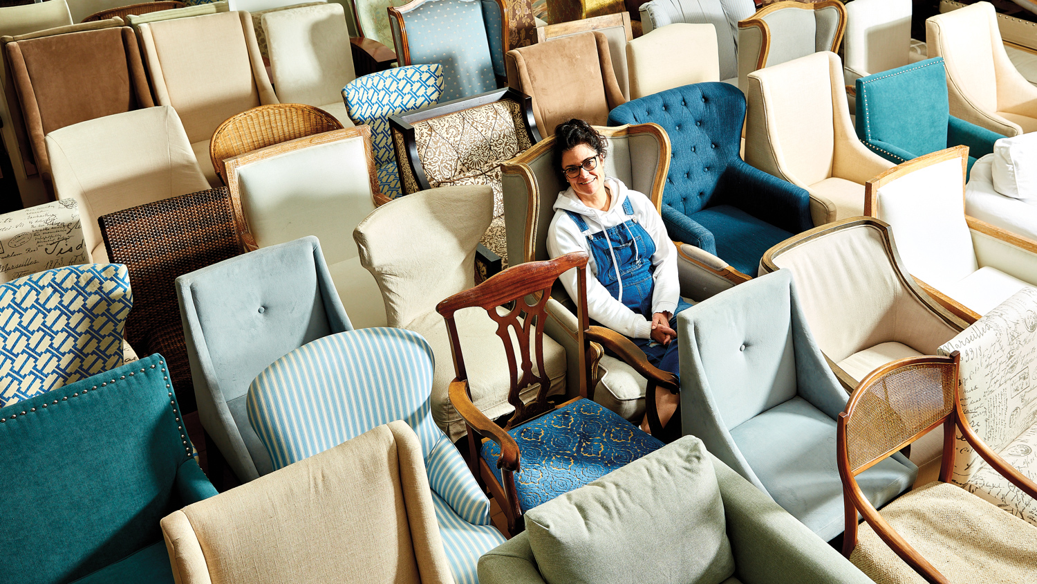 Designer Carolyn Flannery seated amongst rows of different chairs
