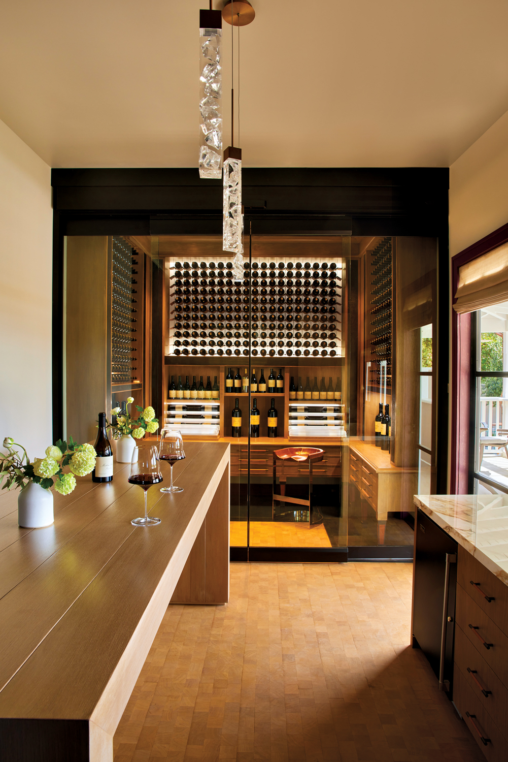 A glass-enclosed wine storage room behind a long wood table.