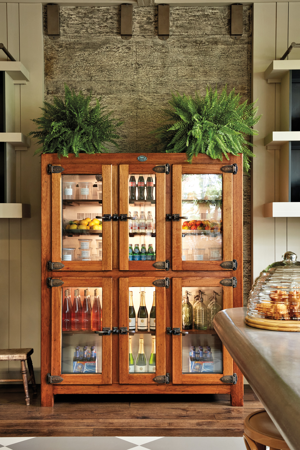 Wooden drink cabinet topped with ferns and set against a textured green wall