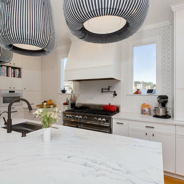A bright, contemporary kitchen with a cohesive white color scheme, including white cabinets, countertops, and a range. The space is illuminated by stylish black pendant lighting fixtures, creating a striking contrast and adding a touch of modern elegance.