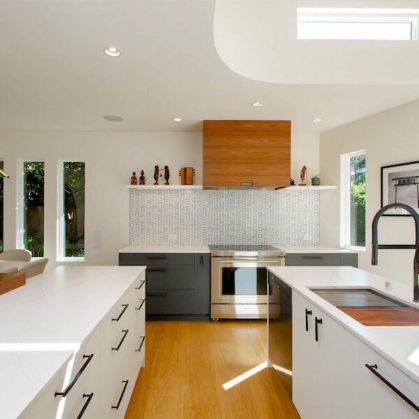 A kitchen with a clean and minimalist design. White cabinets and countertops create a bright and airy atmosphere, complemented by a light wood range that adds warmth to the space. The overall aesthetic is modern and inviting.