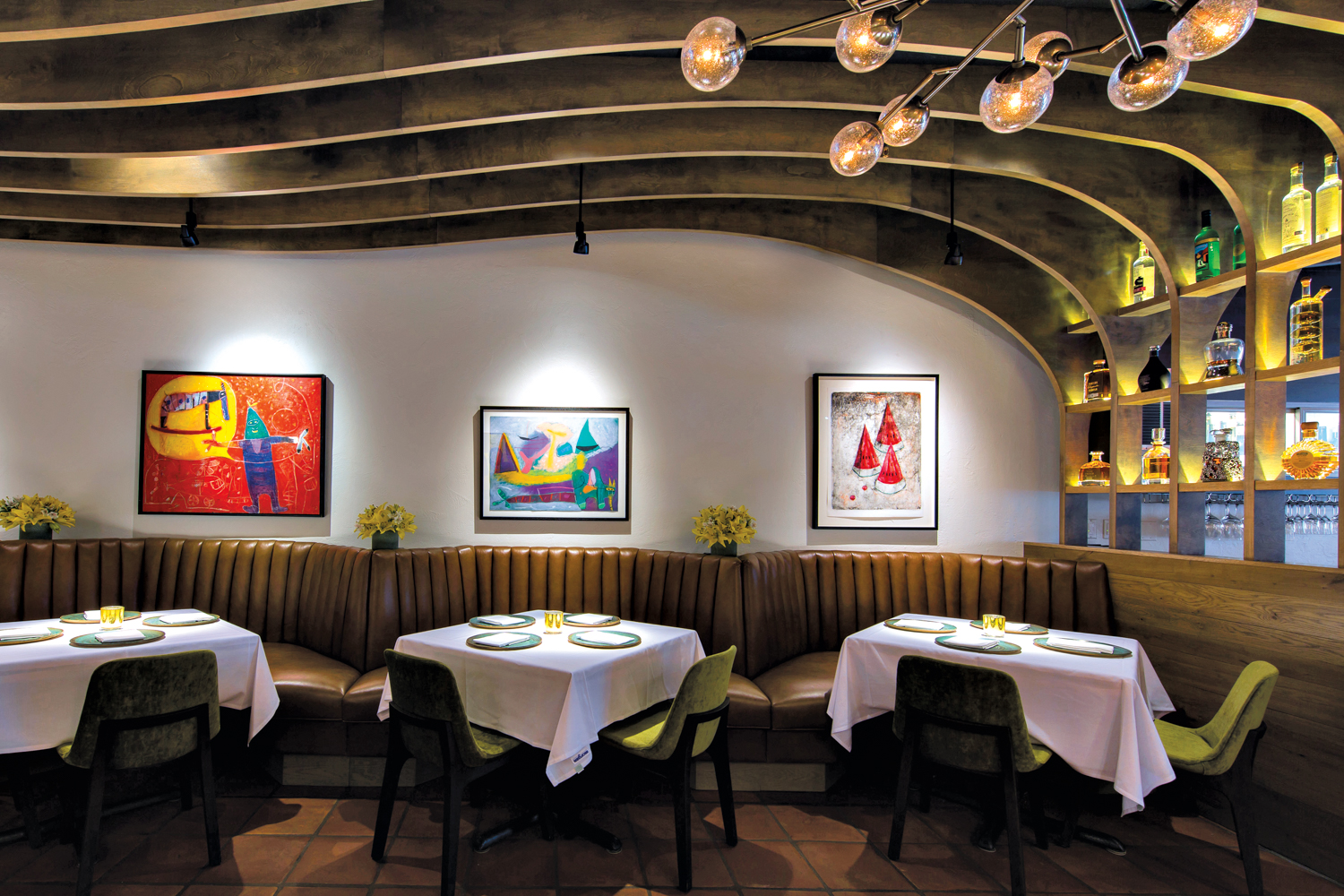 restaurant dining room with tufted leather banquettes beneath colorful artworks