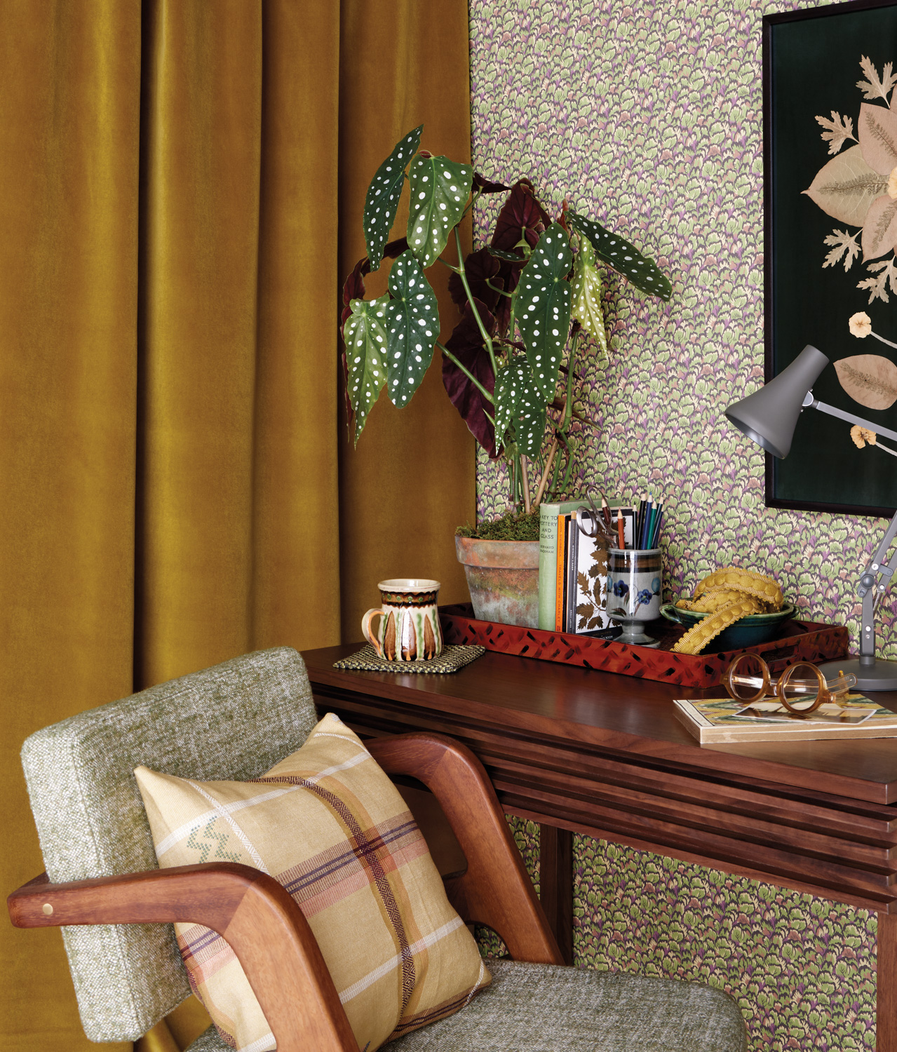 A cozy corner with a wooden desk, green and pink patterned wallpaper, and a yellow velvet curtain
