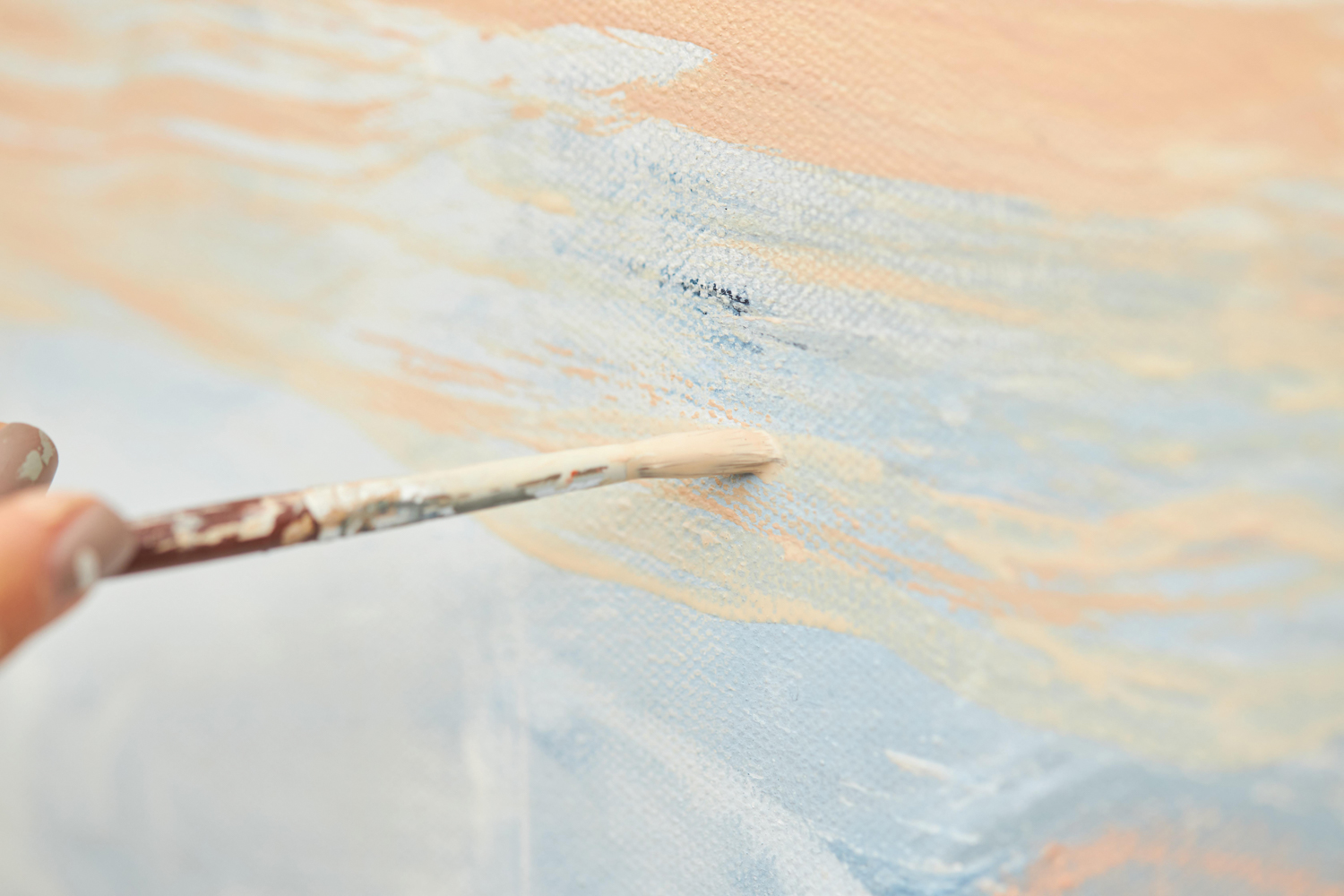 a person strokes a brush against a canvas of abstract light blue and cream paint