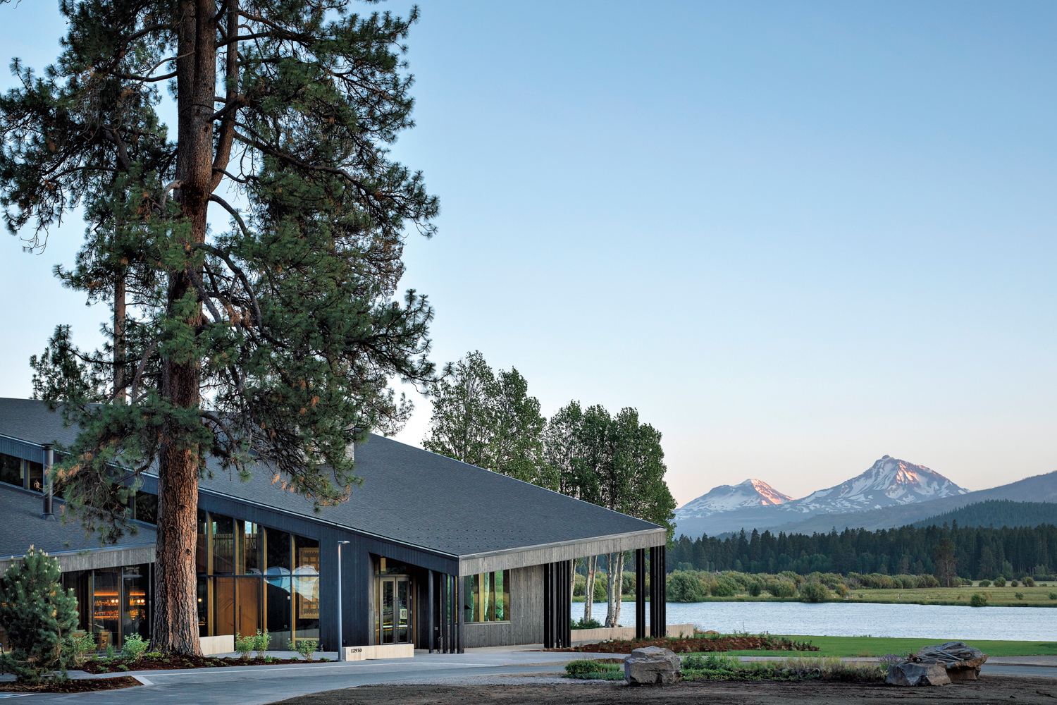 Exterior of building with sloping black roof and expansive glass walls overlooking a lake