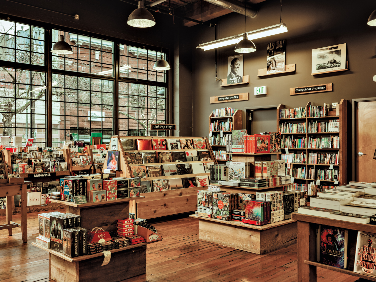 Bookstore with floor-to-ceiling windows, wood floors and wood display cases and tables