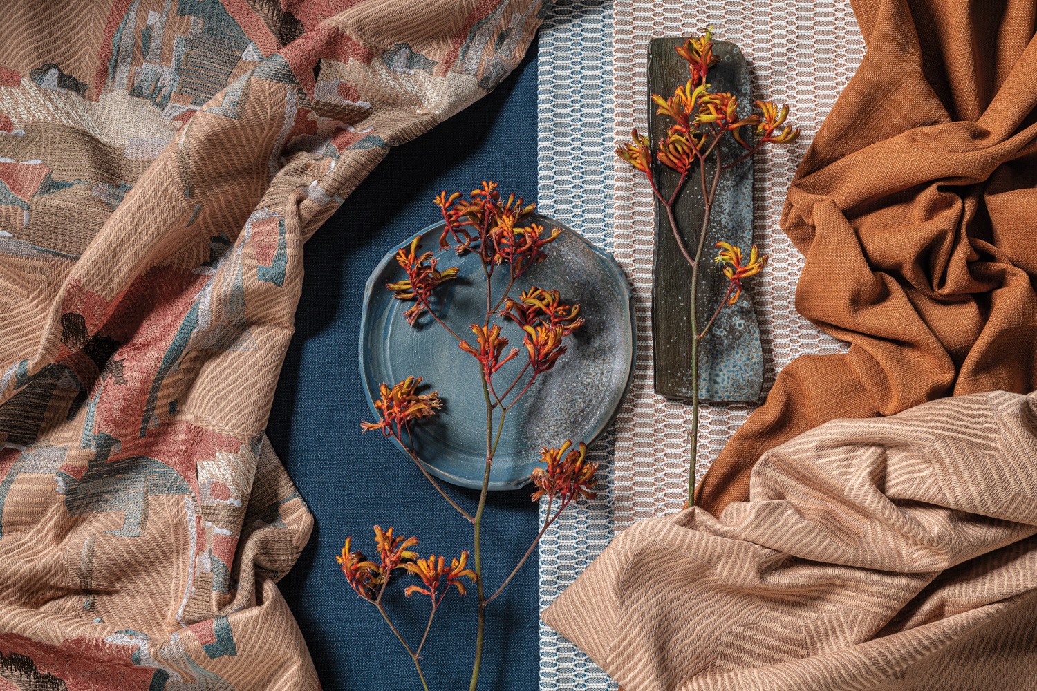 Blue and burnt-orange fabrics topped with dark gray plates and orange-red flowers