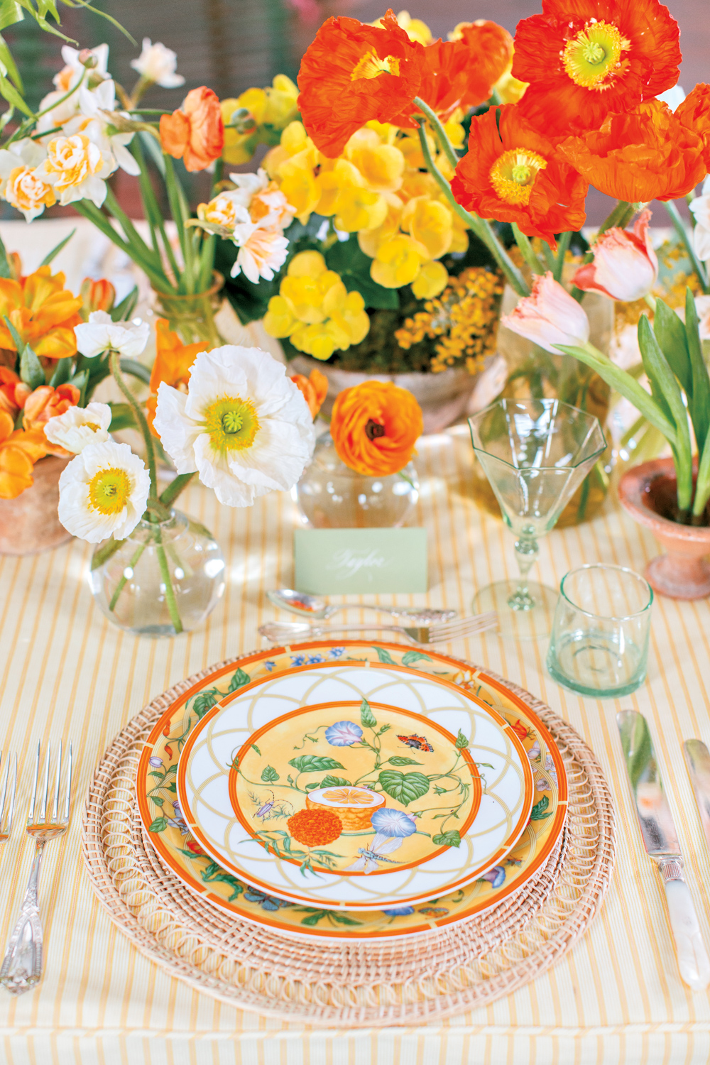 Styled tabletop with yellow and orange floral arrangements and place settings.
