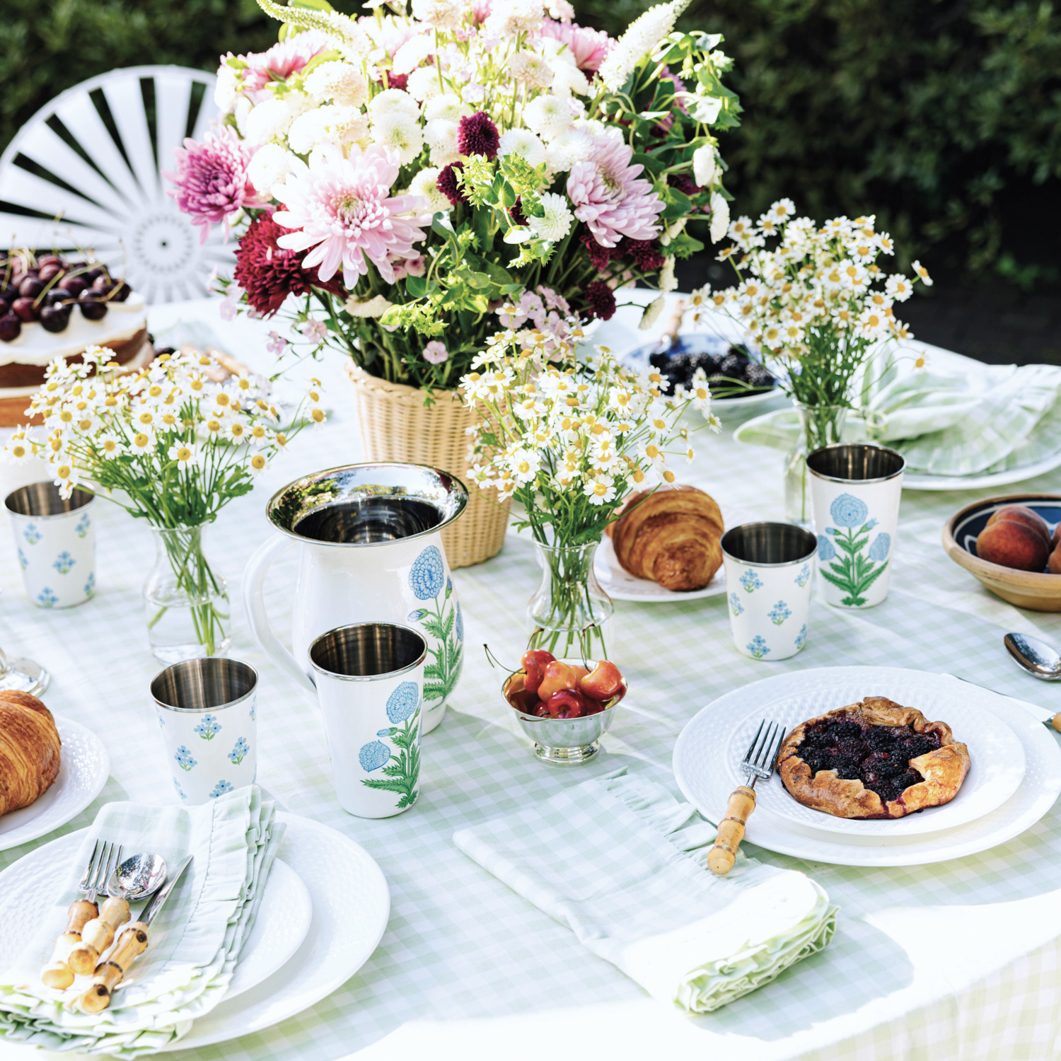 Outdoor tablescape of blue floral stainless-steel cups and light sage green checked napkins and tablecloth. 