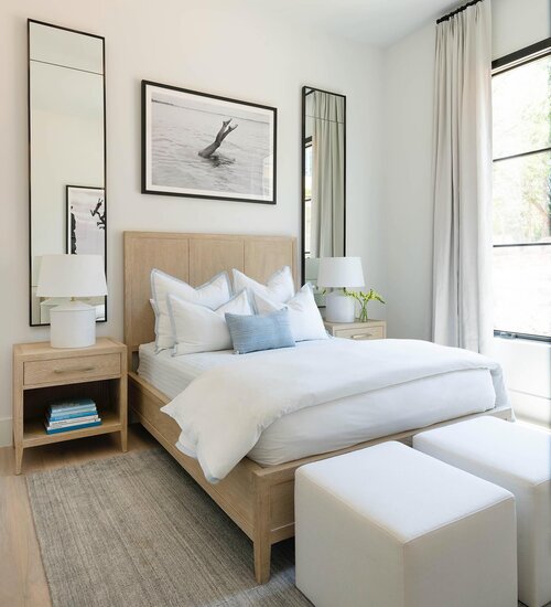 A tidy bedroom with white bedsheets and a big mirrors reflecting the room.