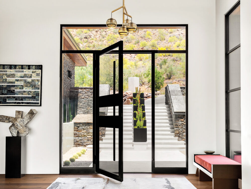 black steel and glass door opens to an entry with a red bench, abstract painting and stone sculpture