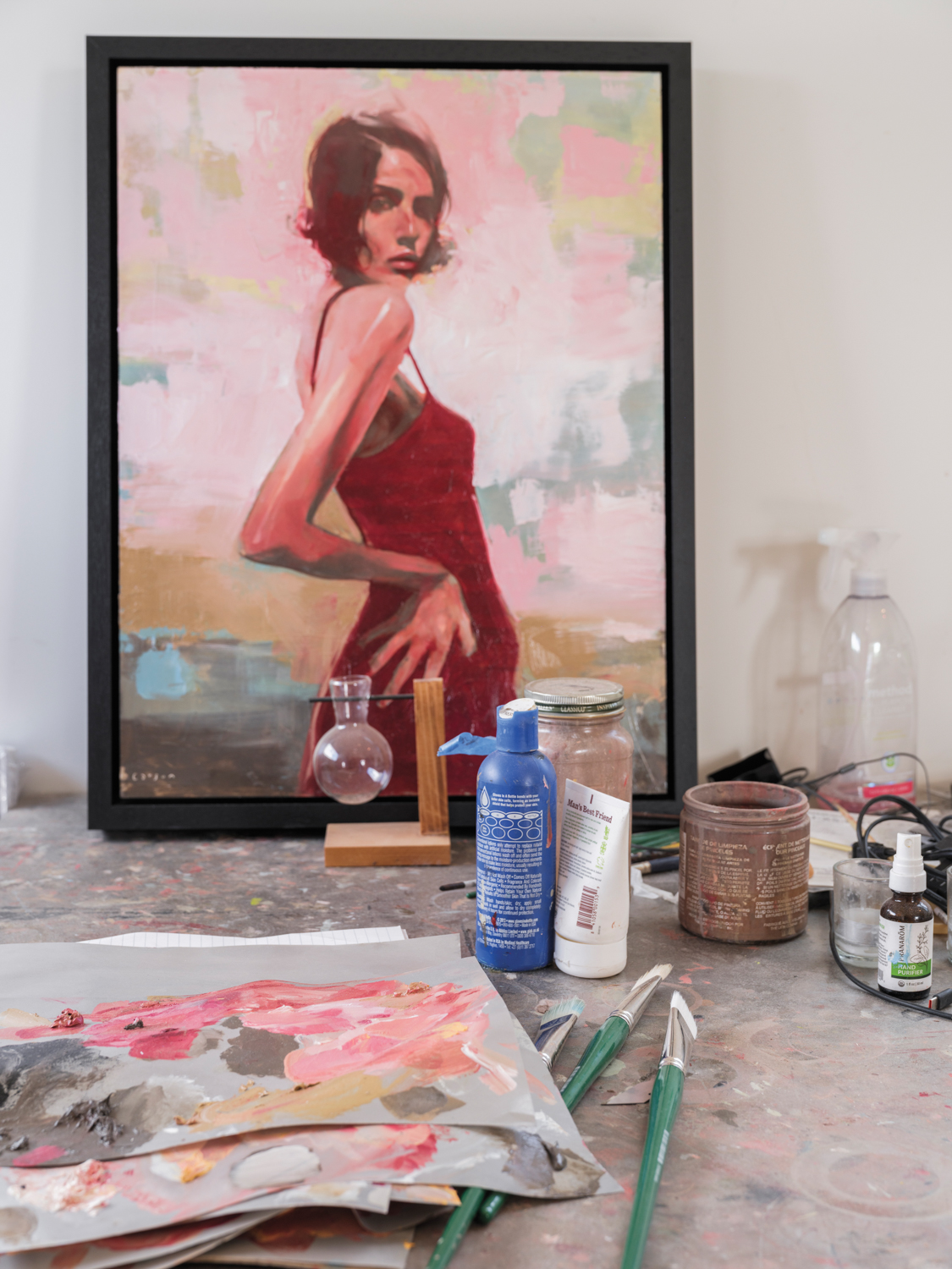 art supplies on a table in front of a painting of a brunette woman in a red dress