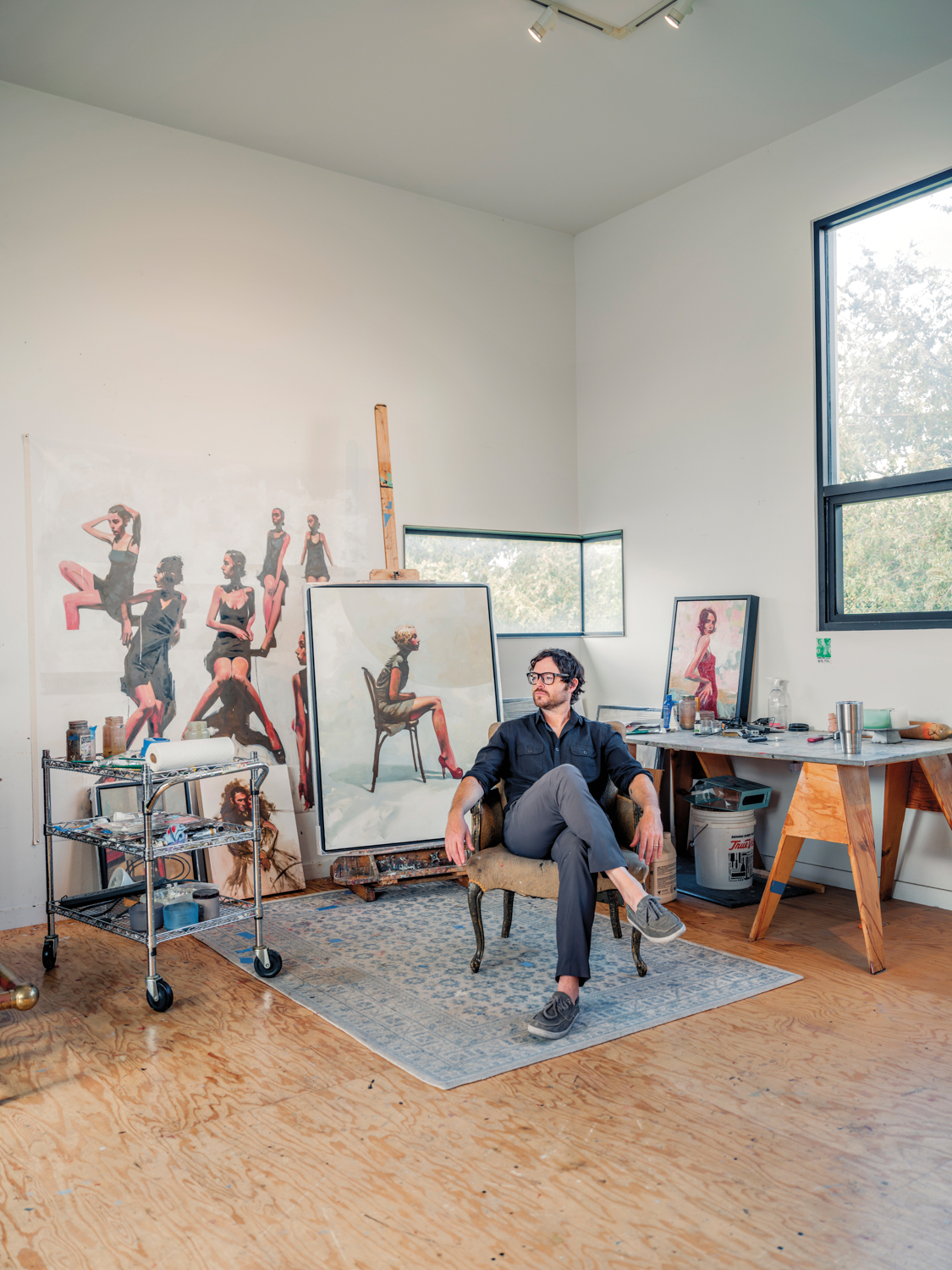 man sitting in chair surrounded by artwork and art supplies