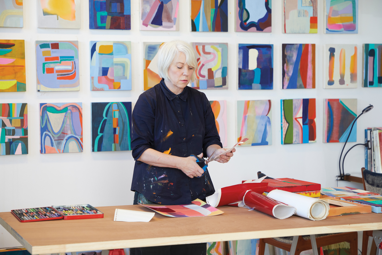artist Anna Kunz cutting paper in front of a grouping of colorful paintings