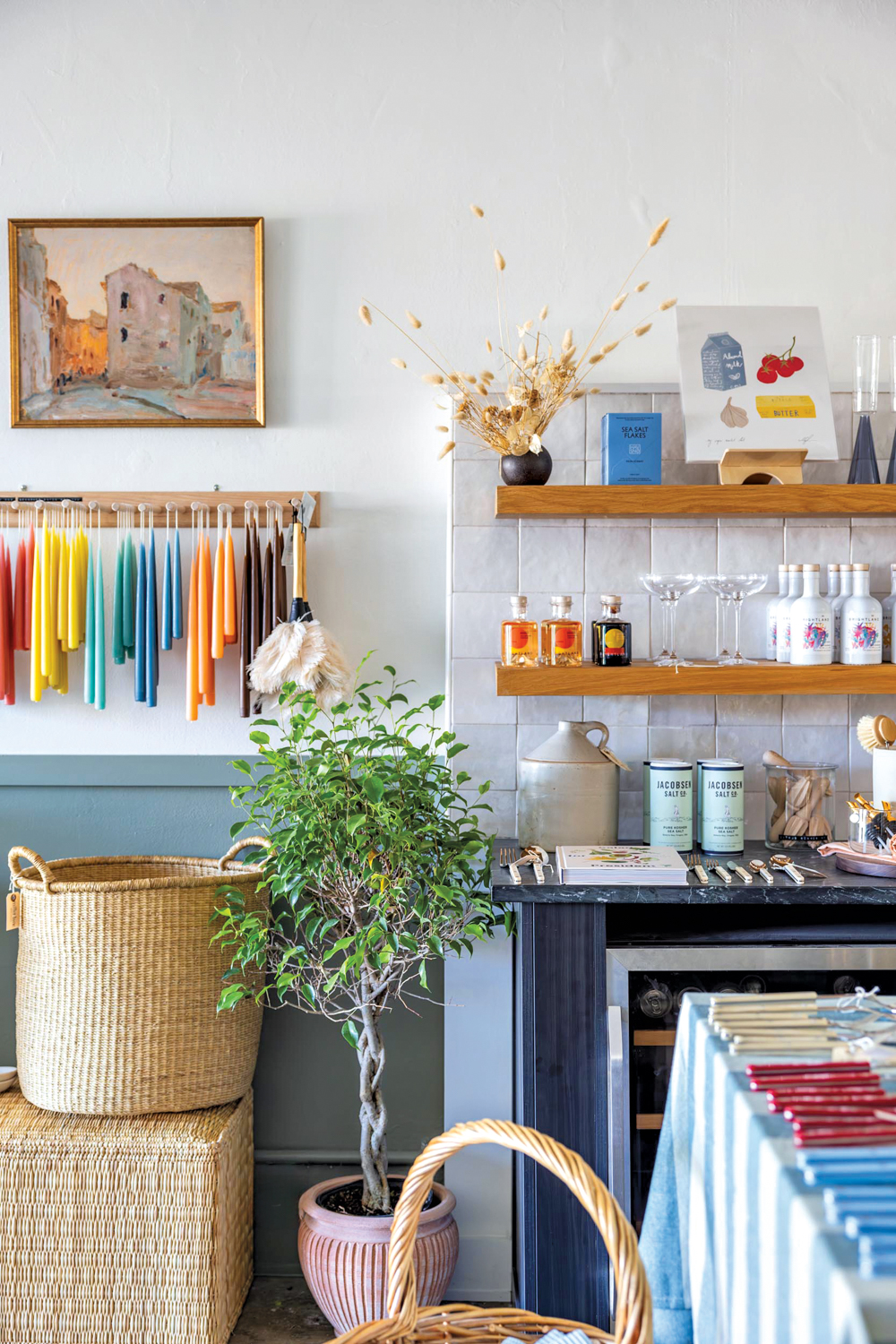 Decor boutique with colorful taper candles hanging on a wall and glassware on shelves.