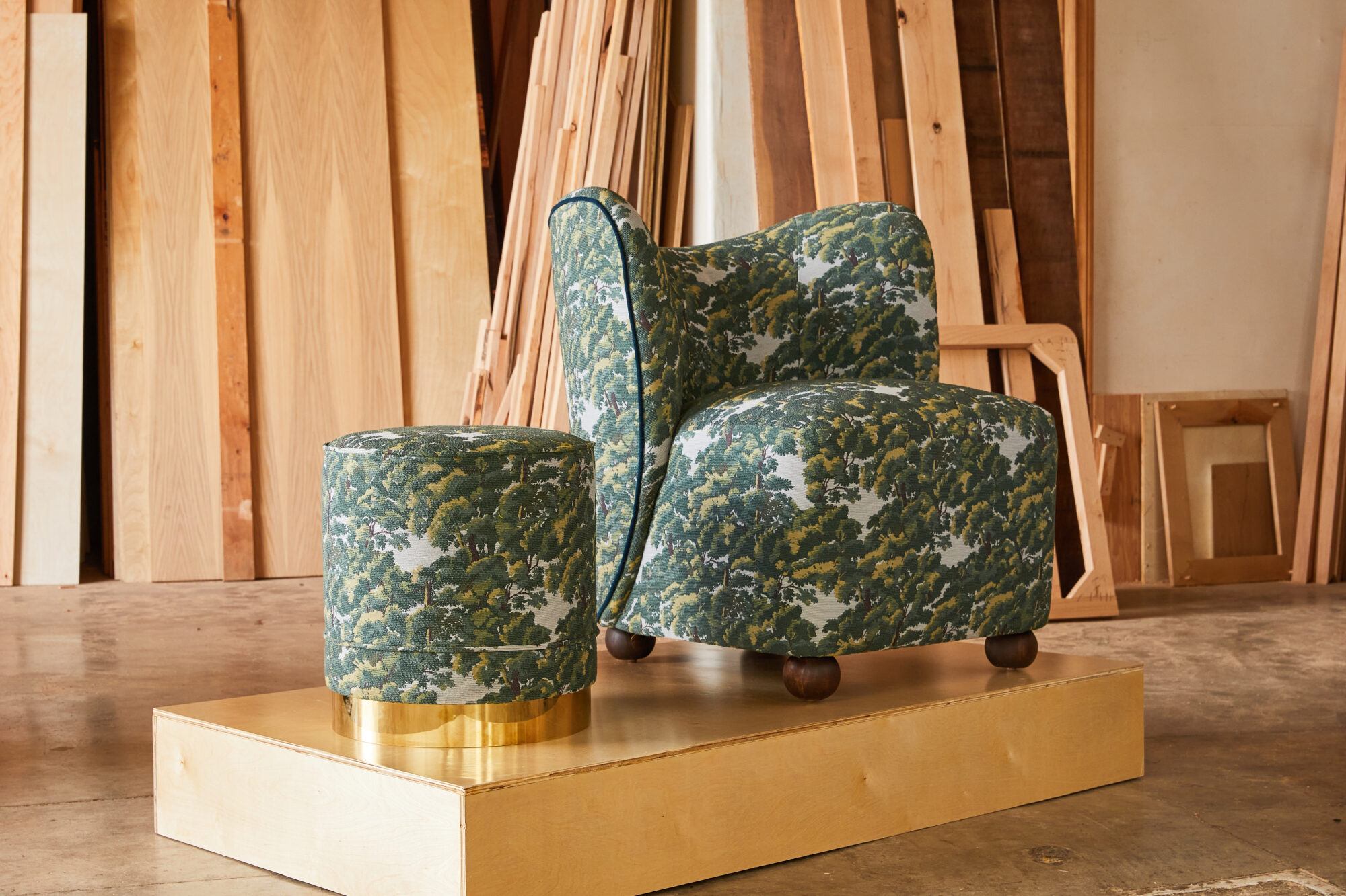 Chair and stool with oak tree-patterned upholstery upon a platform, featured at High Point Market