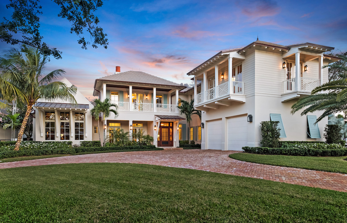 A large white home featuring several balconies over looking a lush yard and perfectly paved driveway.