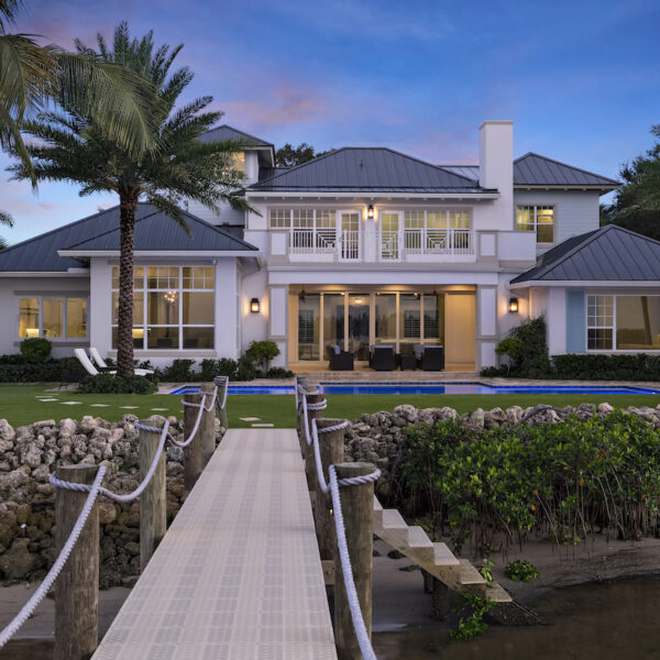 Spacious white house surrounded by palm trees and a dock.