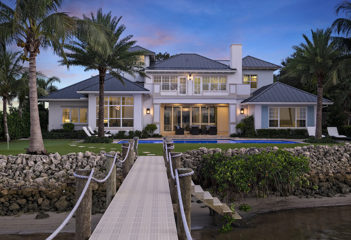 Spacious white house surrounded by palm trees and a dock.