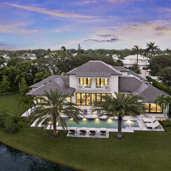 Large luxury home overlooking teal pool with two large palm trees.
