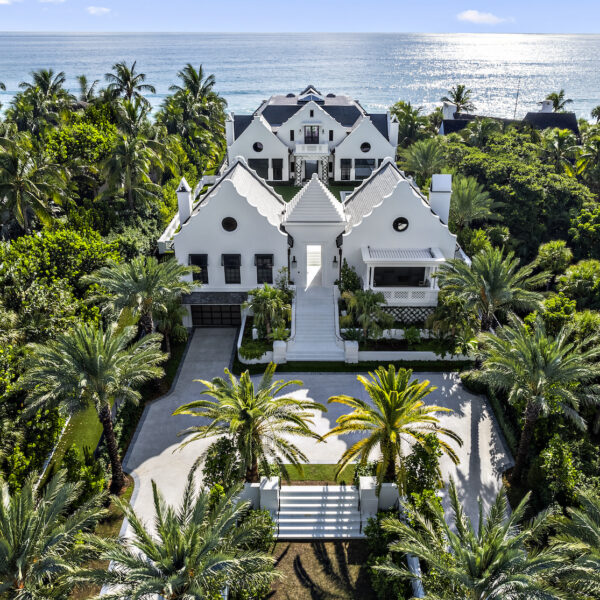 Large white luxury home with large white driveway totally surrounded by palm trees.