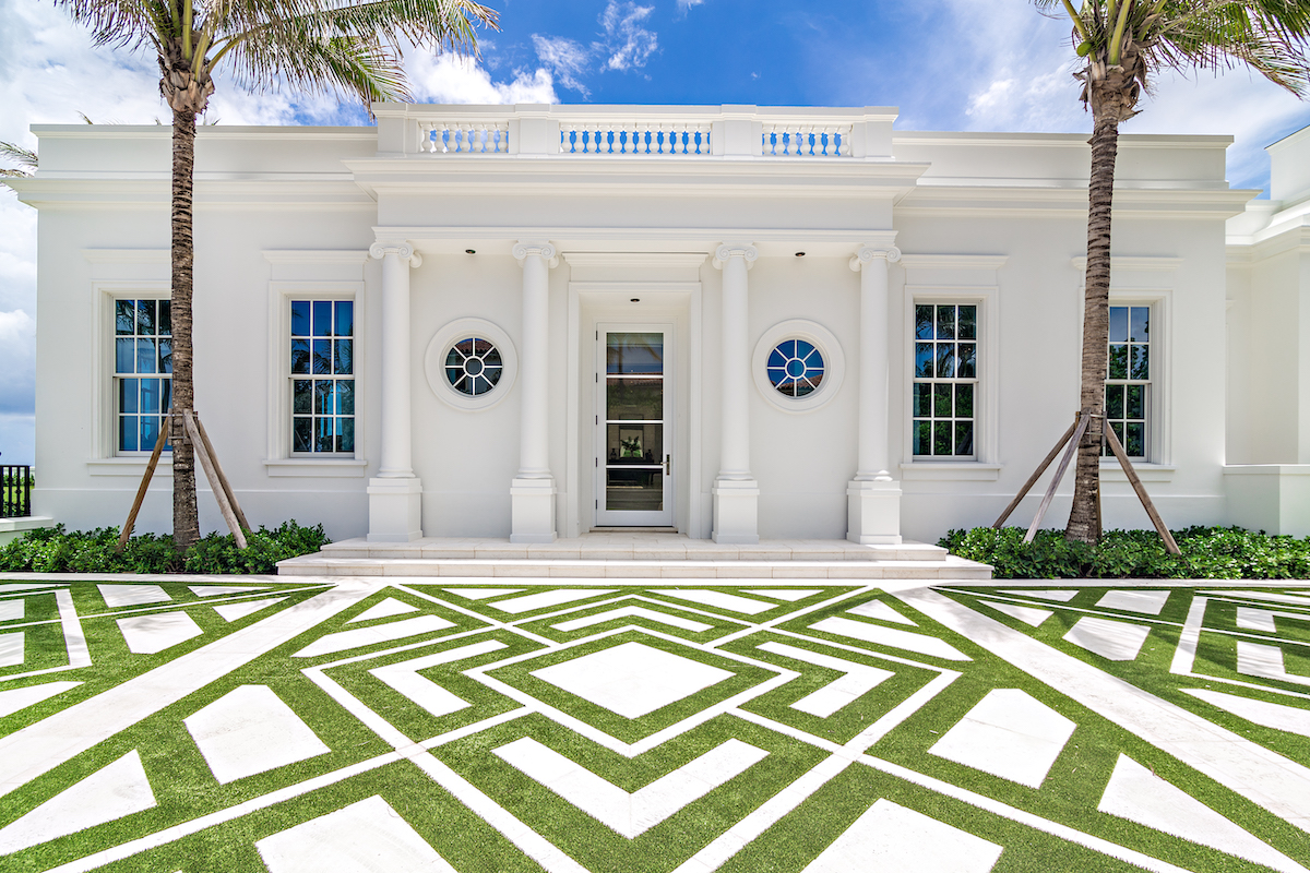 A luxurious white mansion surrounded by palm trees and lush green grass.