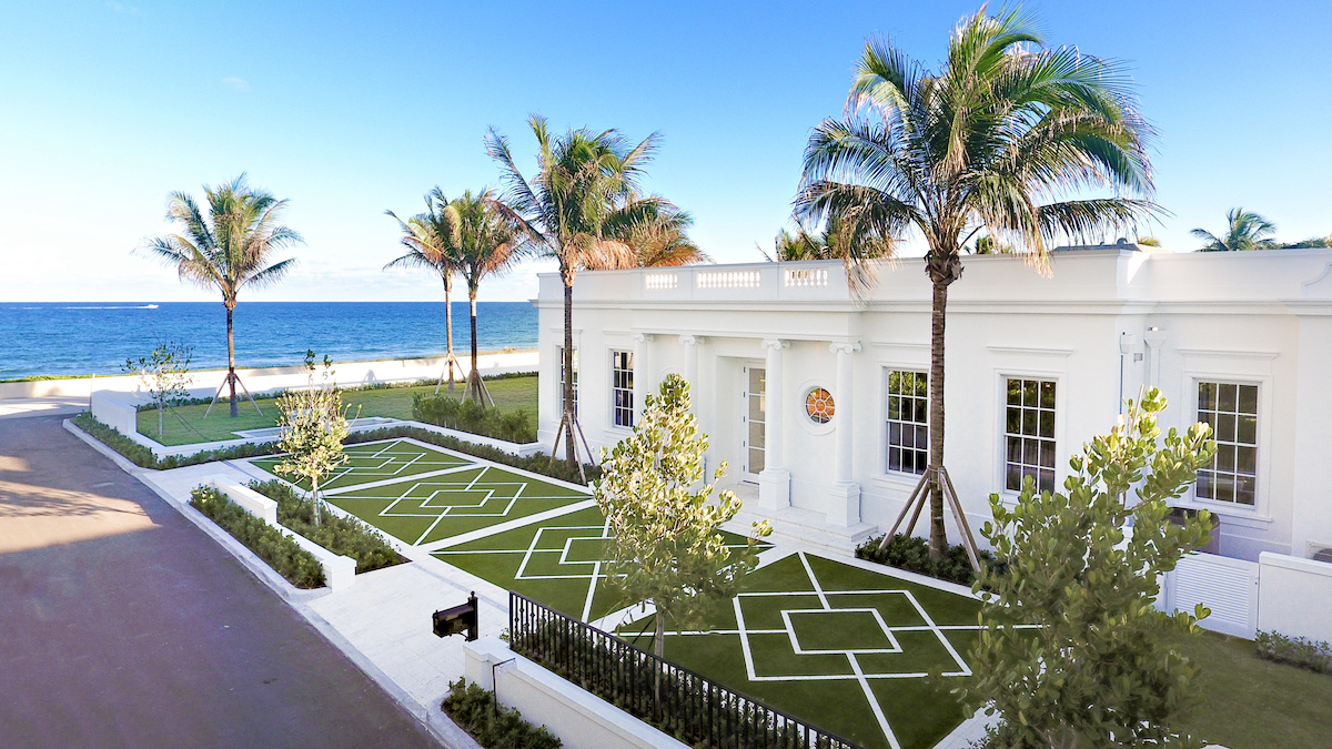 A white house surrounded by palm trees and a well-maintained lawn.