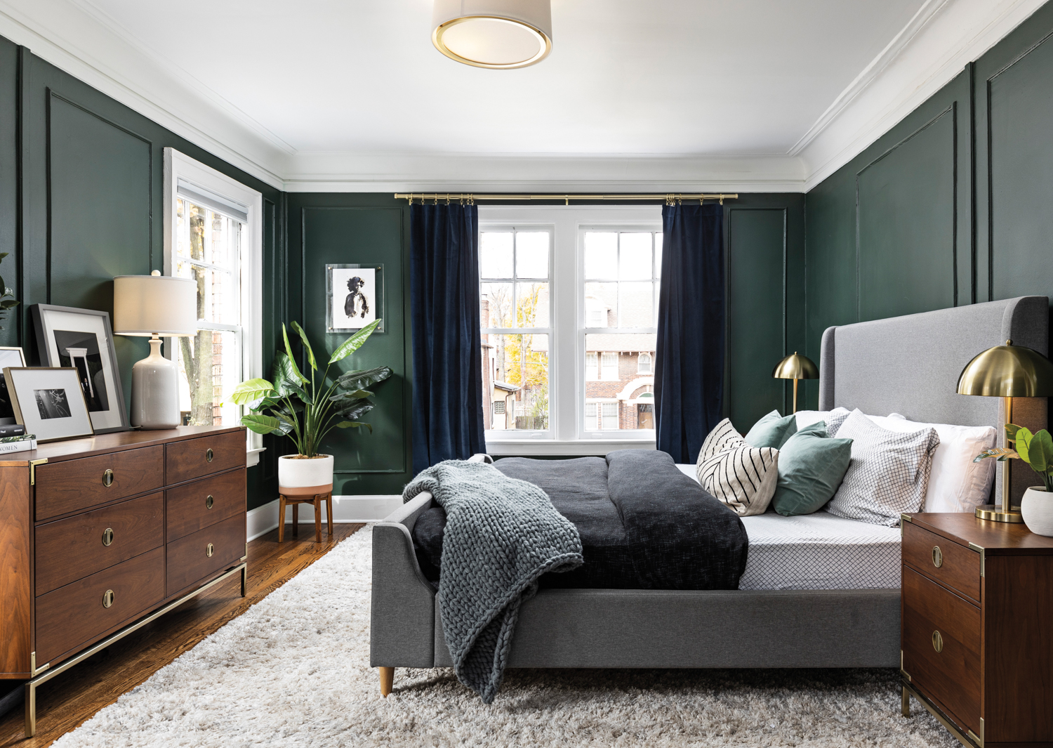 Bedroom with dark green walls, gray upholstered bed and fluffy white area rug on wood floors.