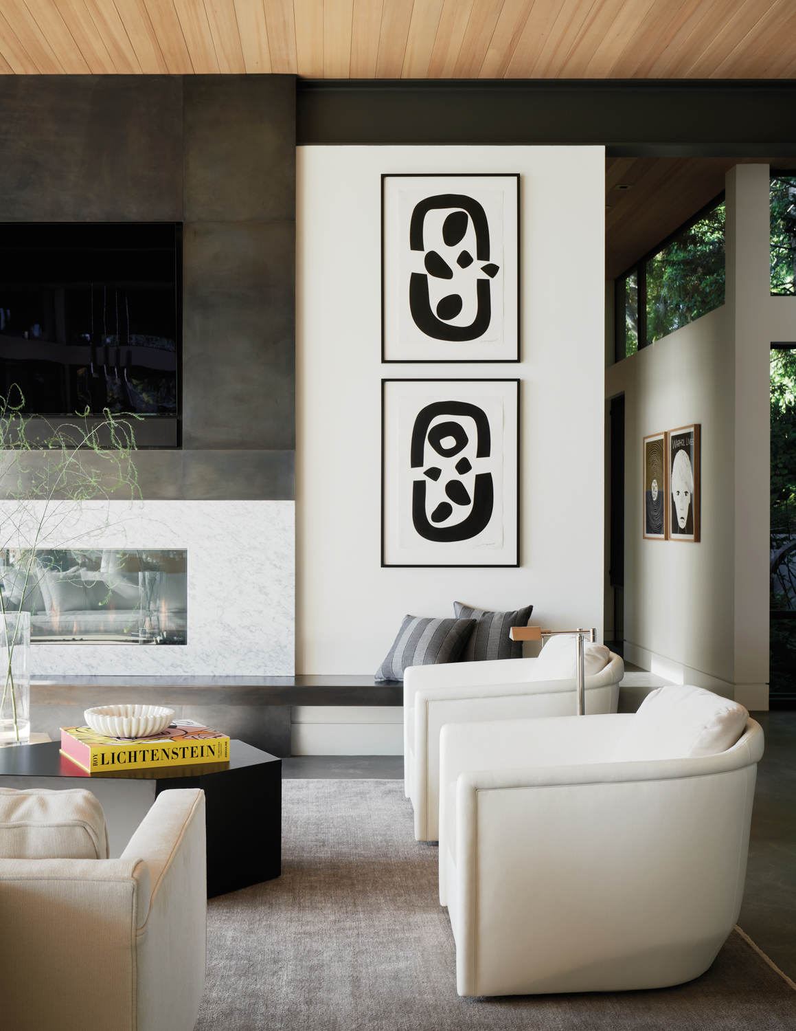 Living room with white armchairs facing black coffee table in front of modern artwork and fireplace