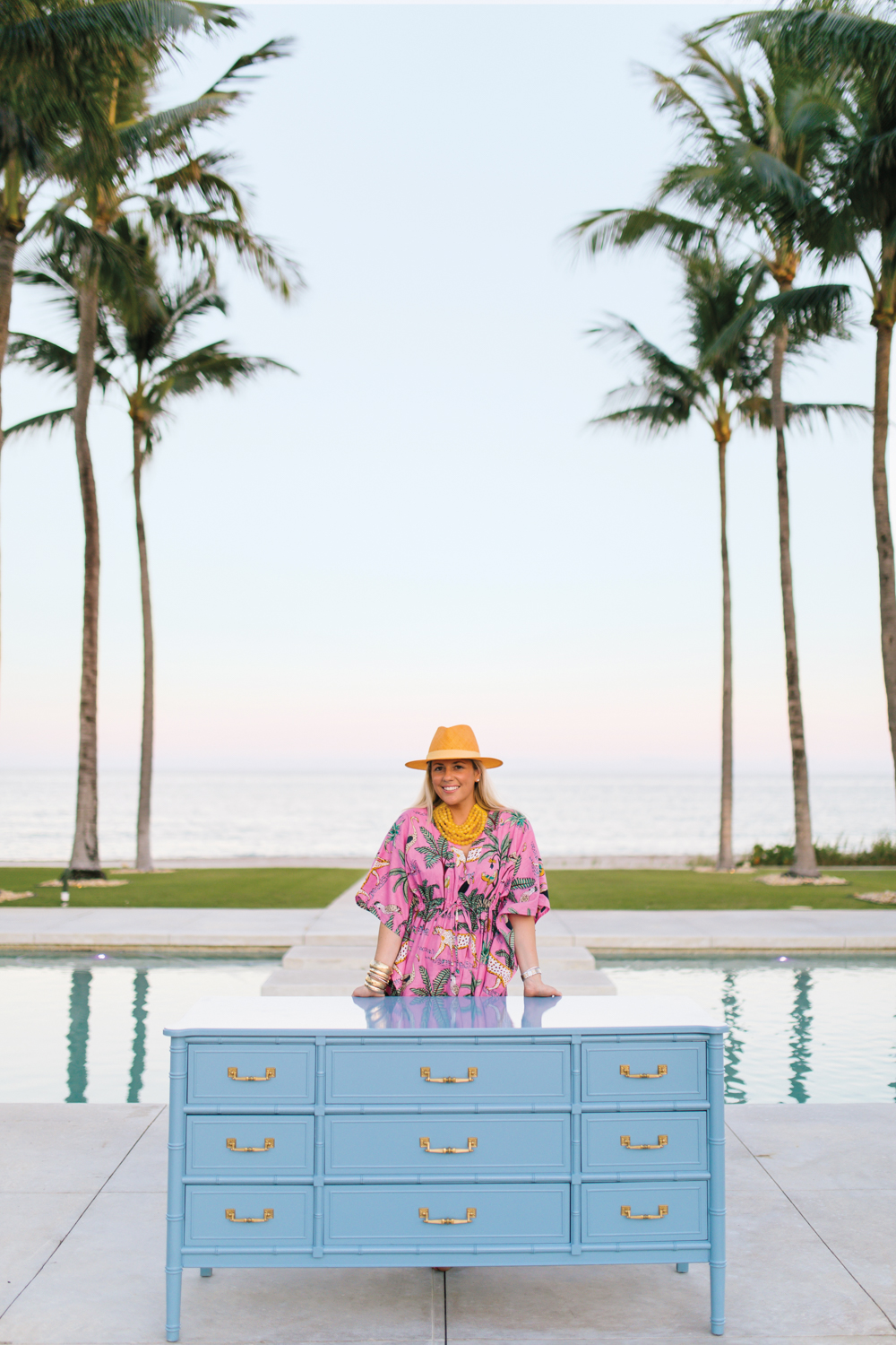 Elizabeth Hutchinson stands behind a blue-lacquered dresser on a pool patio