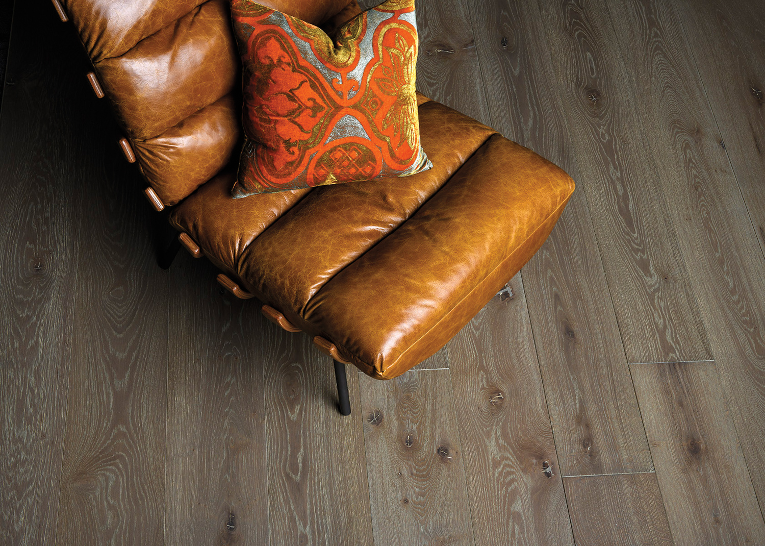 leather lounge chair with an orange-patterned pillow atop wooden floors