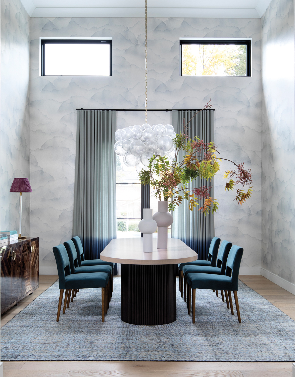 Dining room with cloud-like wallpaper, glass bubble chandelier and blue-upholstered chairs