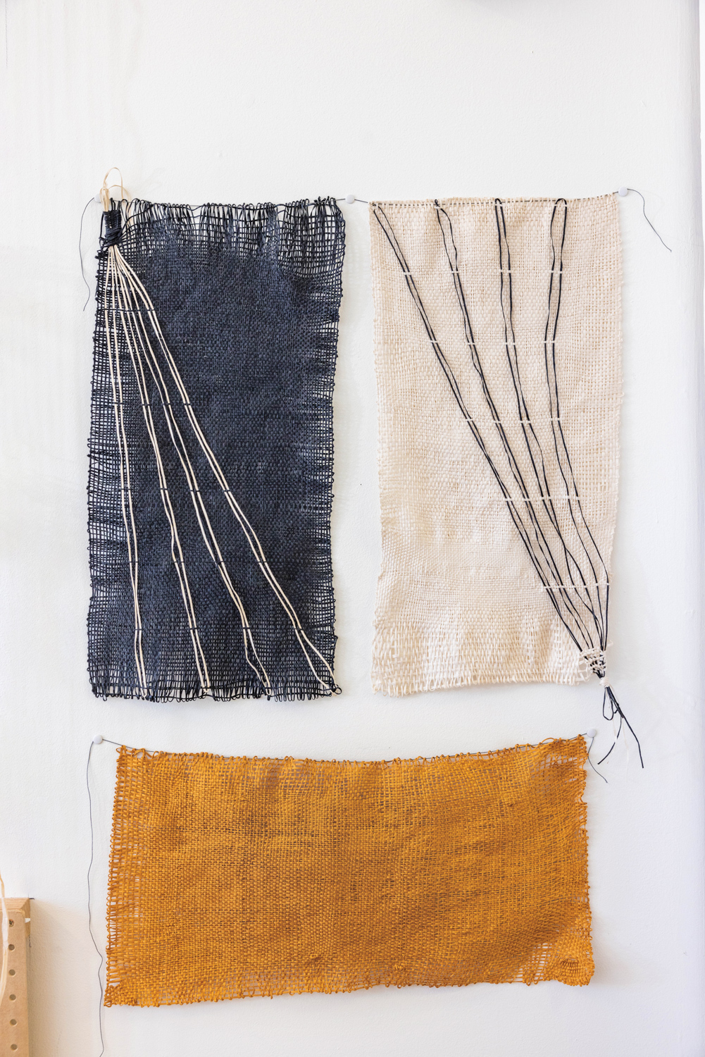 three freeform woven textiles hanging on a white wall