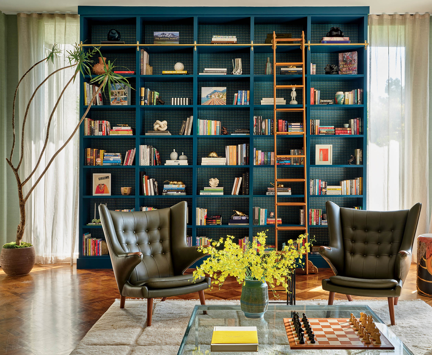 dark blue built-in with a rolling ladder behind green leather armchairs