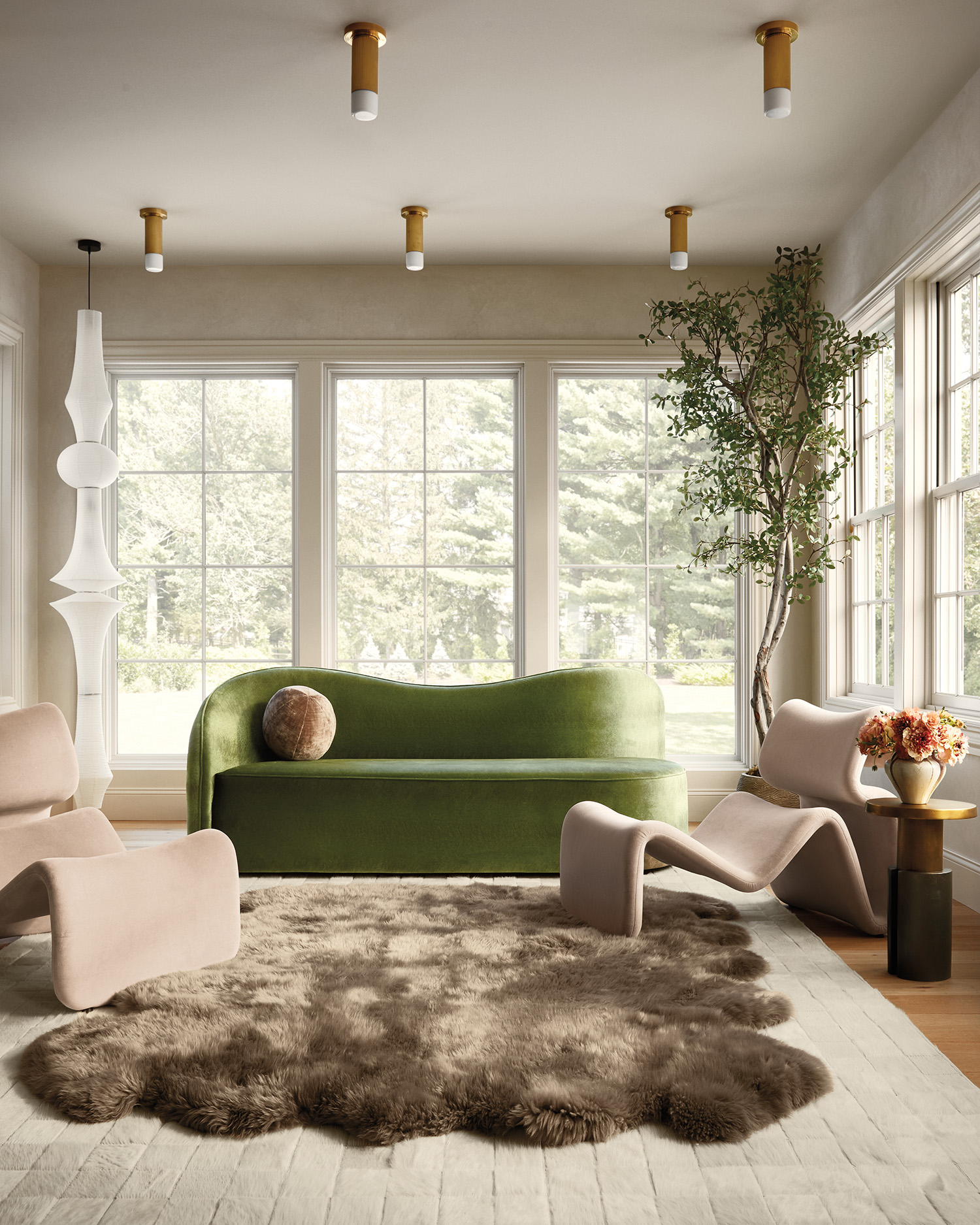 Living room with green velvet sofa, curved beige lounge chairs, sheepskin rug, and large windows.