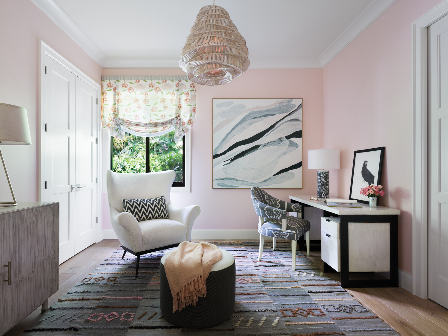 office with pink walls, patterned rug, white armchair, black and white desk and gray-toned artwork
