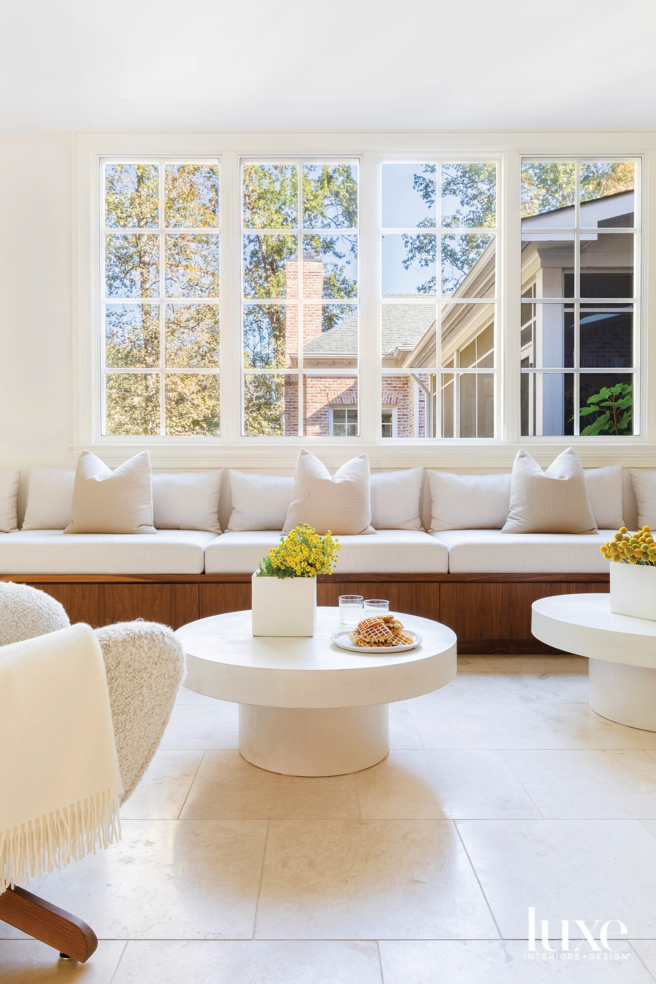 Large window above built-in banquette with round coffee tables