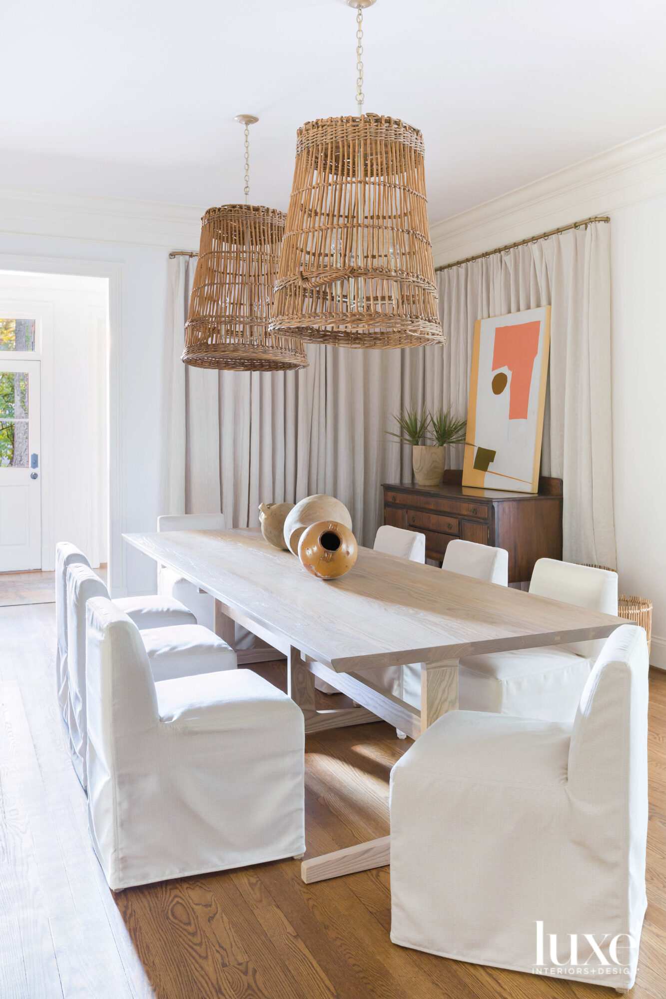 Dining room table with slipcovered chairs and basket-style pendants