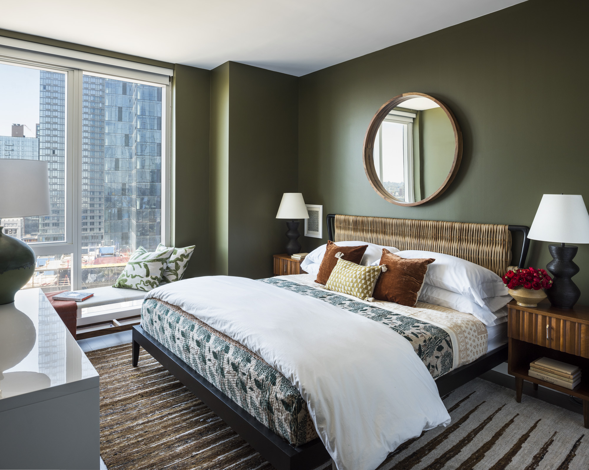 green bedroom with bed with rattan headboard and circular mirror