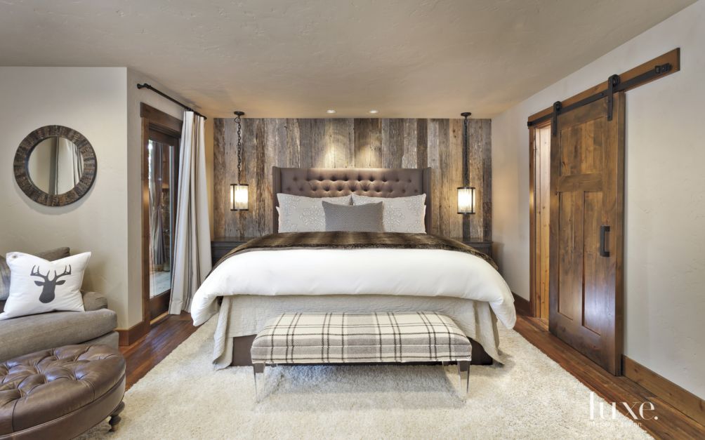 wood barn door slides across entry to rustic primary bedroom with plaid bench