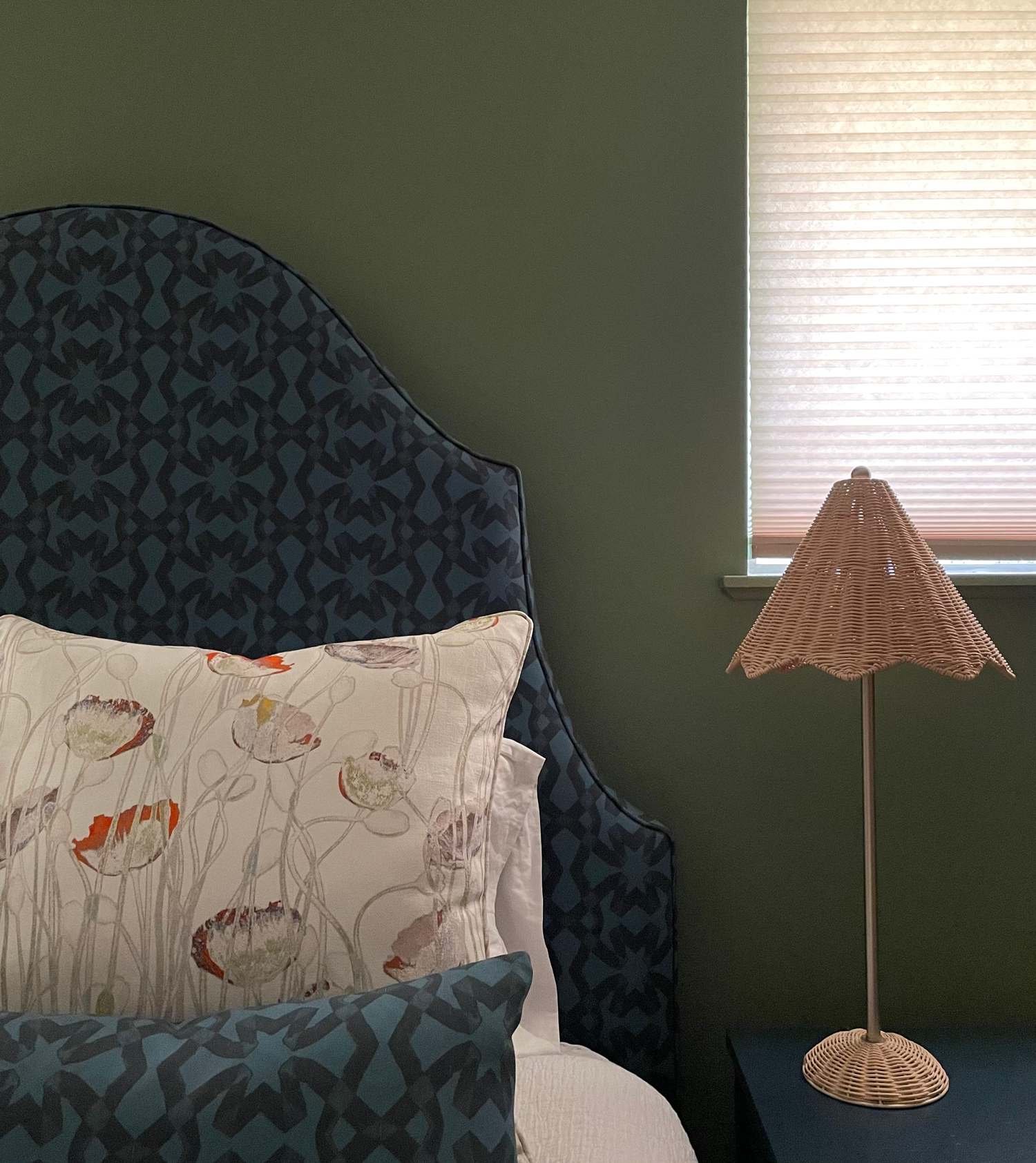 green bedroom with bed with blue headboard and rattan lamp