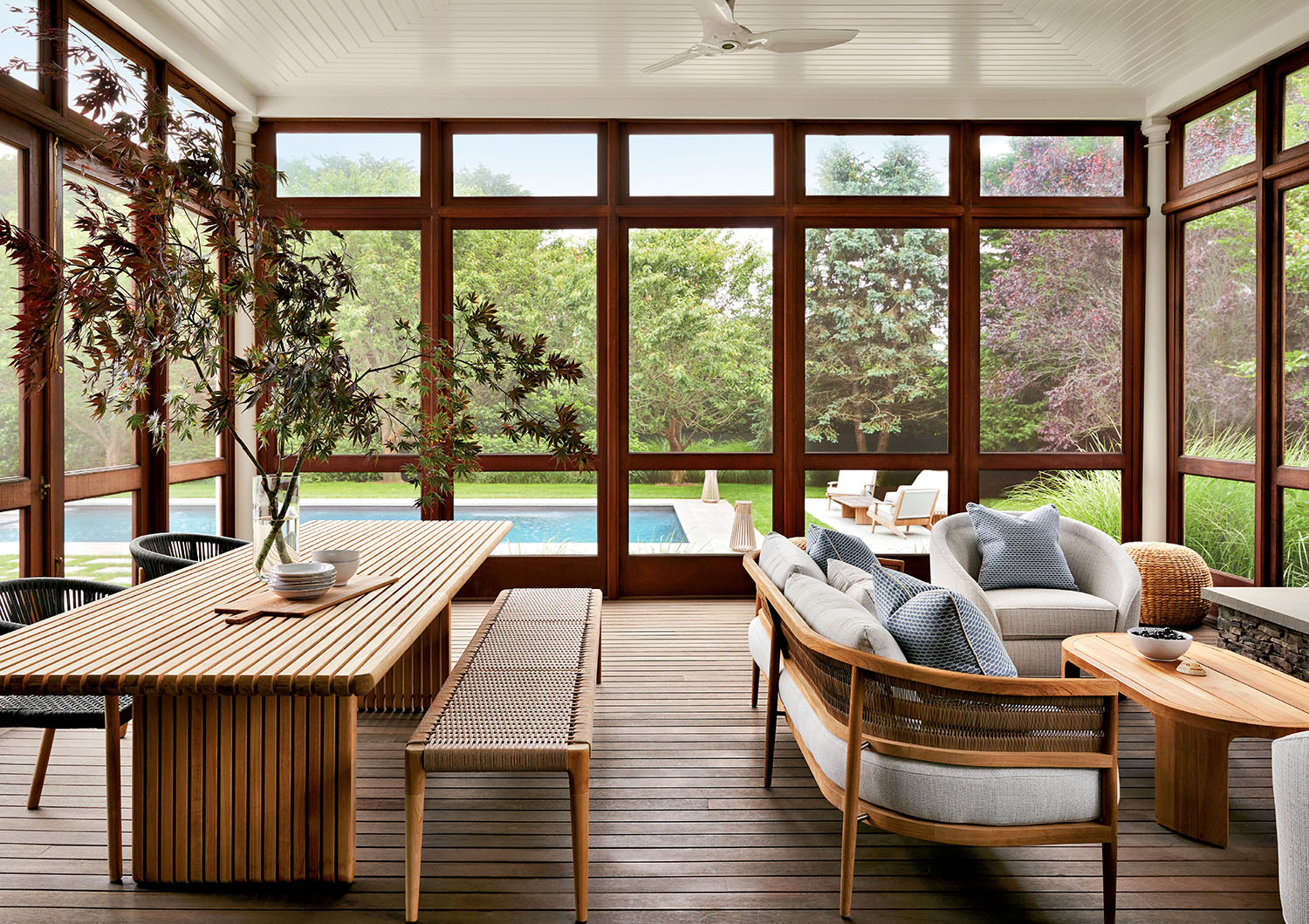 A screened porch with wooden furniture overlooks a backyard with a pool, green lawn, and outdoor seating area.