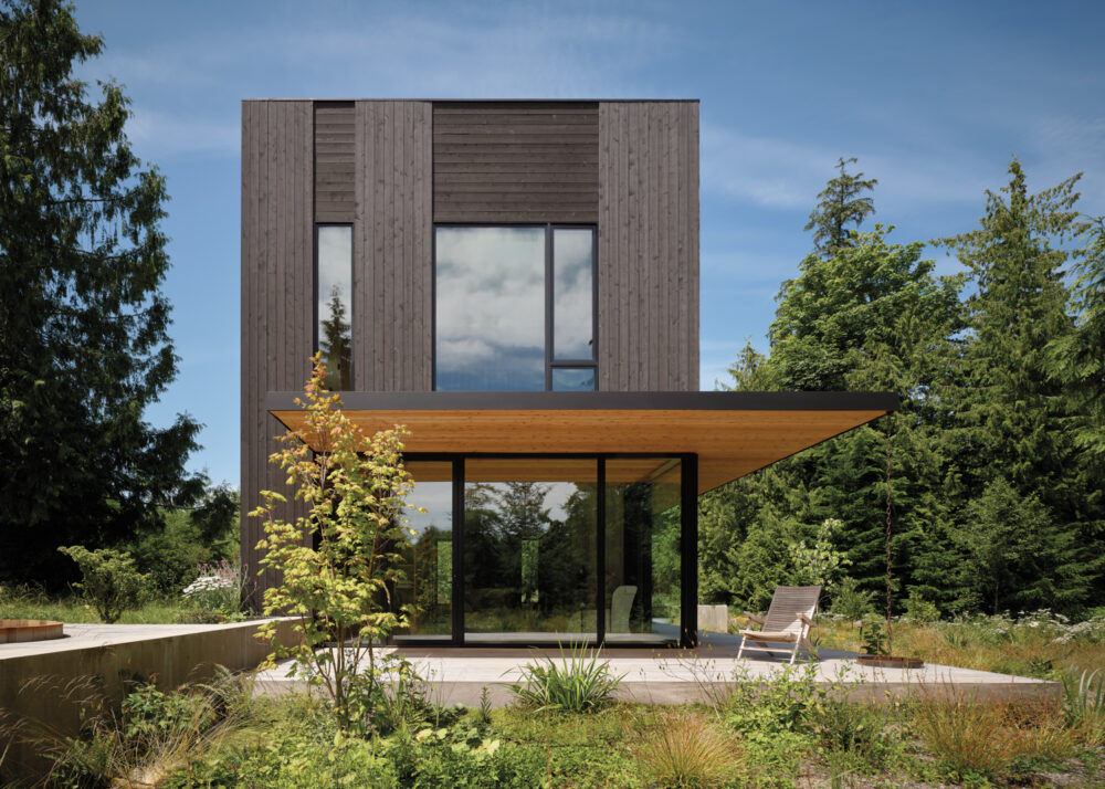 A sleek modern house with a spacious wooden deck and a vibrant landscape