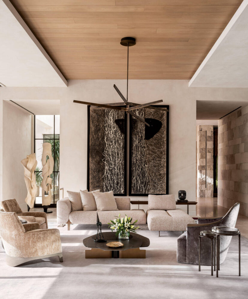 Modern living room with neutral-toned furniture, large abstract artwork on the wall, sculptural decor, a round coffee table, and a minimalist ceiling fan.