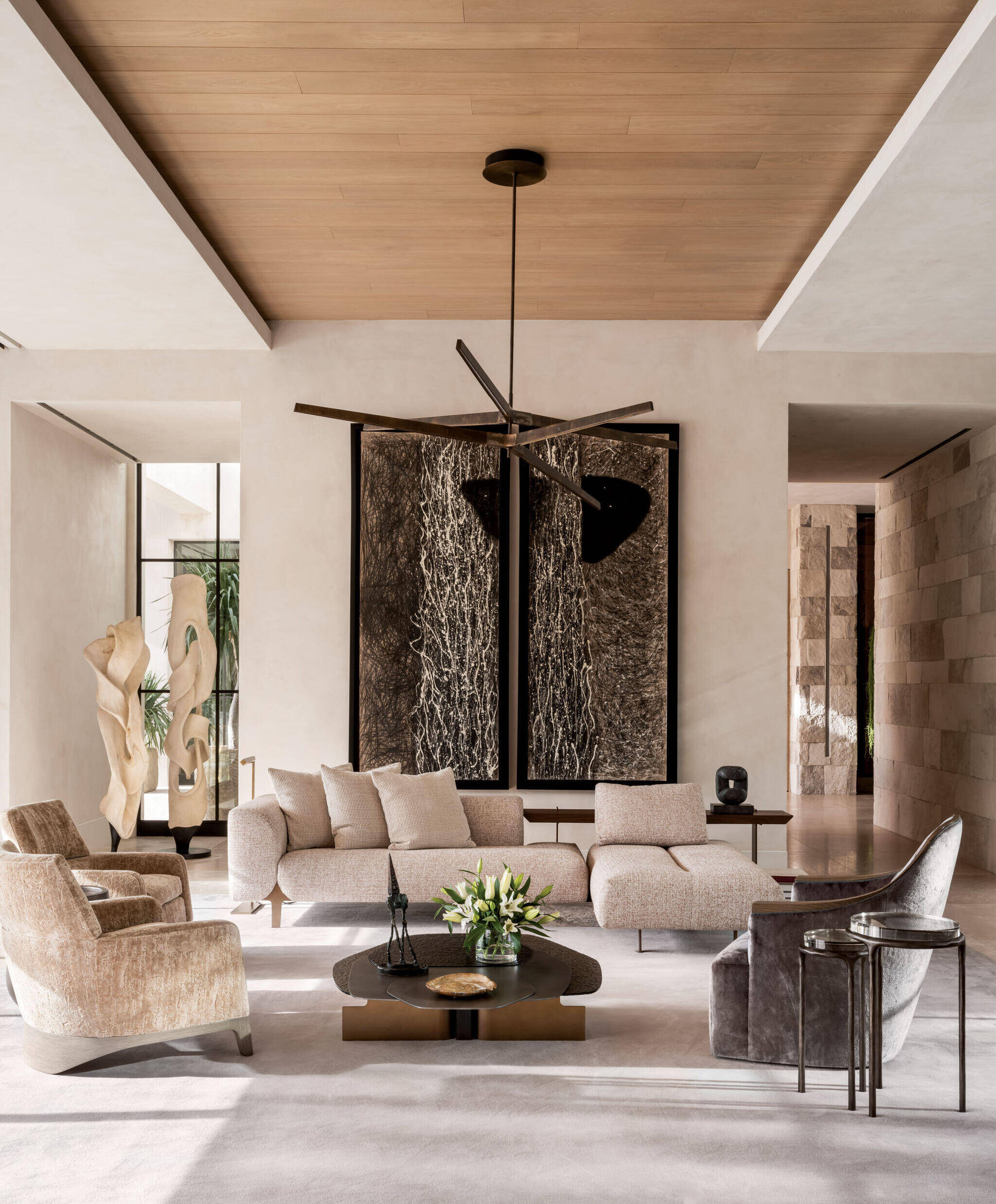 Modern living room with neutral-toned furniture, large abstract artwork on the wall, sculptural decor, a round coffee table, and a minimalist ceiling fan.