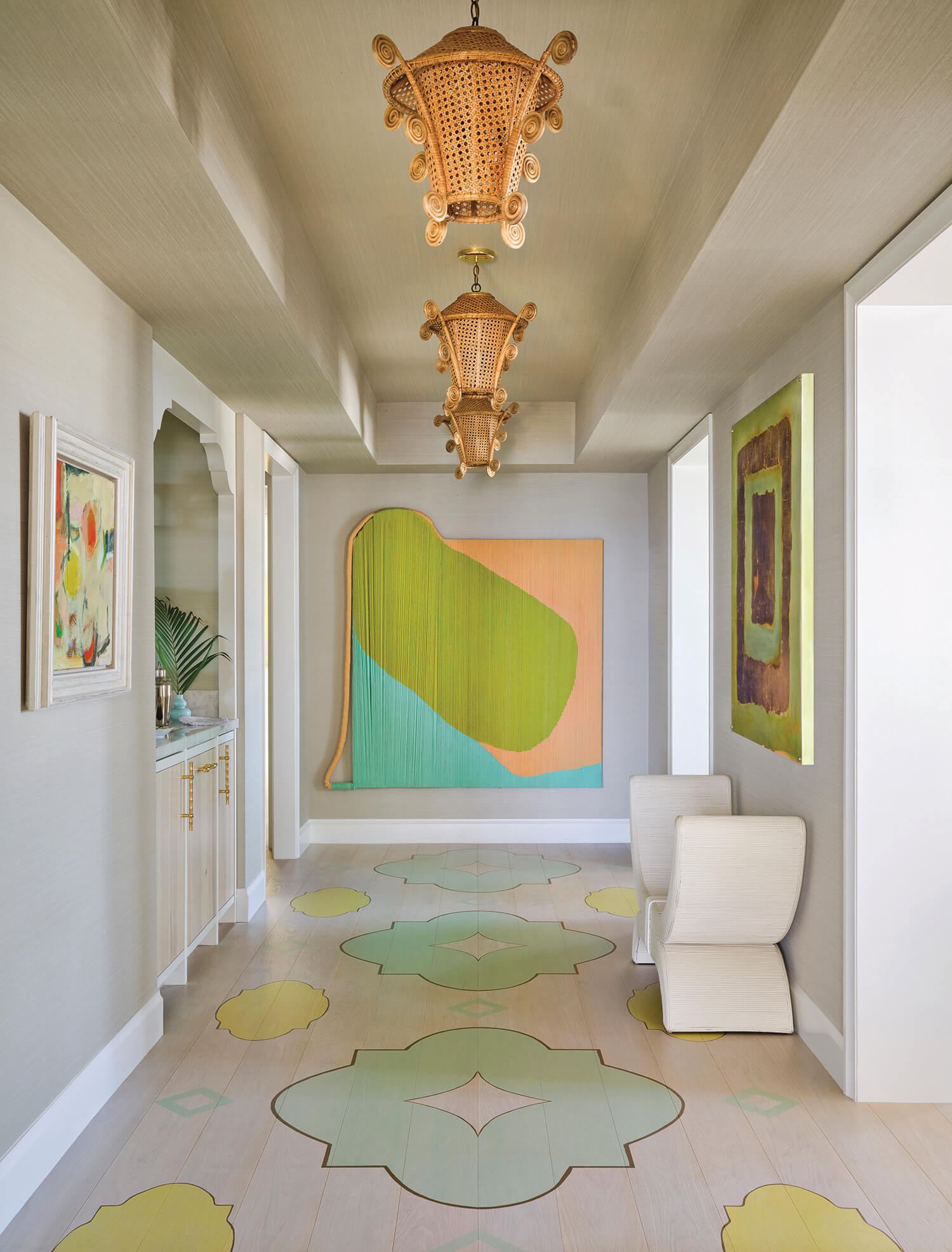 A hallway with modern art on the walls, decorative light fixtures on the ceiling, patterned flooring, and two white sculptural chairs.