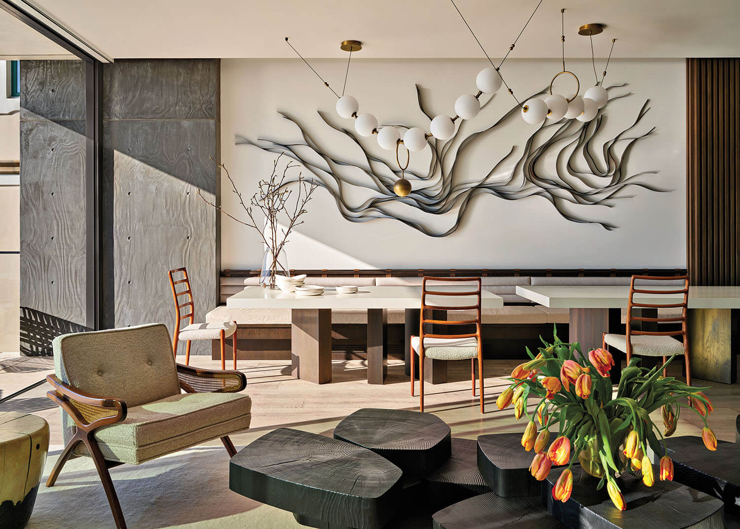 Modern living-dining room with abstract wall art, wooden chairs, a stone-like table, and tulips in a vase on a black coffee table.