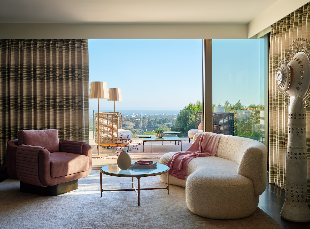 Modern living room with plush seating, round coffee table, and large windows overlooking a scenic outdoor view with clear sky and distant landscape.